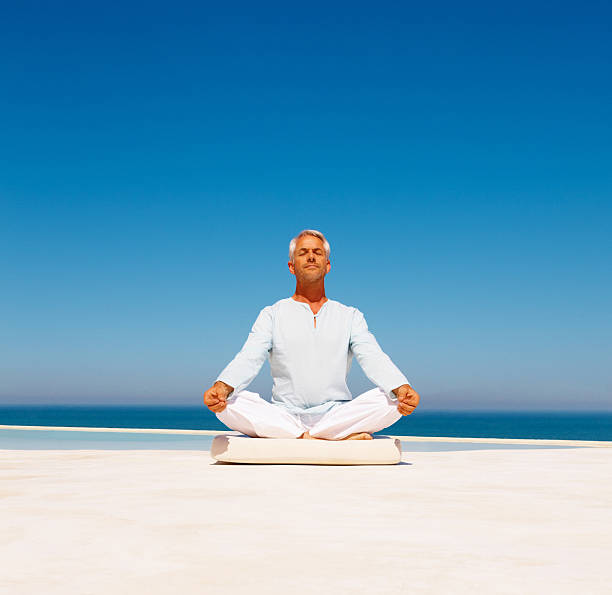 istock Mature man meditating on beach 151539392