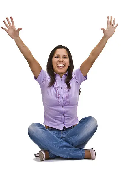 Happy young woman sitting with her legs crossed and arms in the air isolated against a white background.
