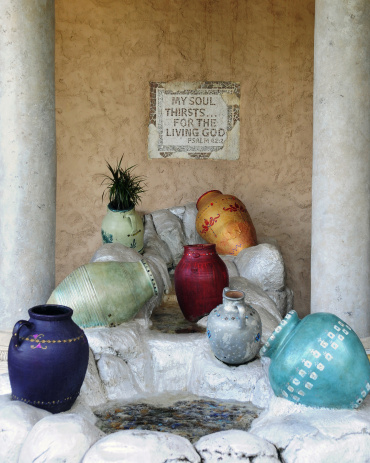 A display of colorful pots by small pools of water between pillars.  A sign in the background says 