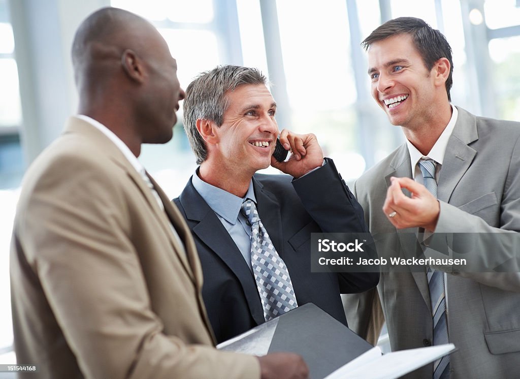 Empresarios divirtiéndose mientras colega talking on cellphone - Foto de stock de 40-44 años libre de derechos