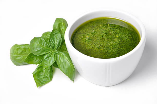 White bowl of basil pesto with fresh basil leaves on left Freshly made green pesto with basil on white background pesto sauce stock pictures, royalty-free photos & images