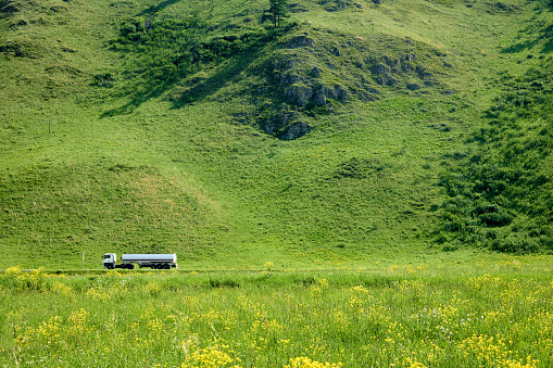Large truck with a cistern drives along the highway on a sunny summer day among the green hills. Transportation of goods on beautiful mountainous terrain