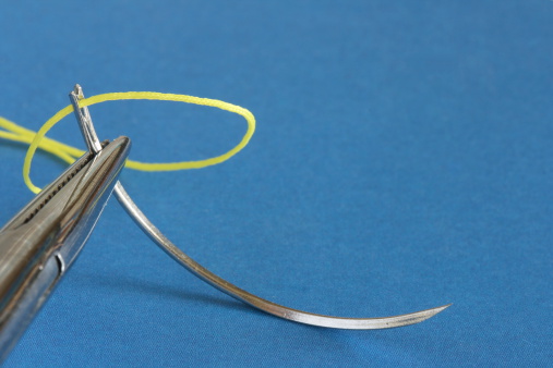 Surgical instrument with needle and thread on blue texture