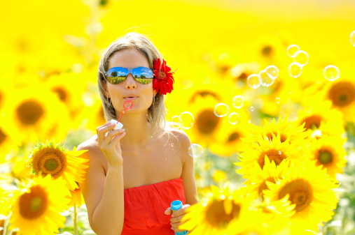 beautiful young woman blowing soap bubbles on blooming sunflower field in summer