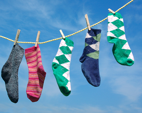three odd socks and one pair of socks hanging on a clothes line. Shot from below so that the sky is the only background.