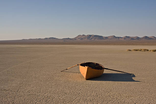 row boat in desert orange row boat in a dry lake bed, in the desert with mountains in the background and clear sky. lake bed stock pictures, royalty-free photos & images