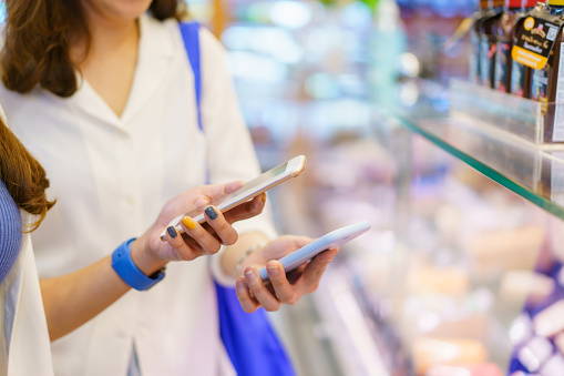 Happy 2 Asian women enjoy walking together around the grocery - department store and using their smartphone to make an online banking transaction to other, secured online banking and money transfer innovation.