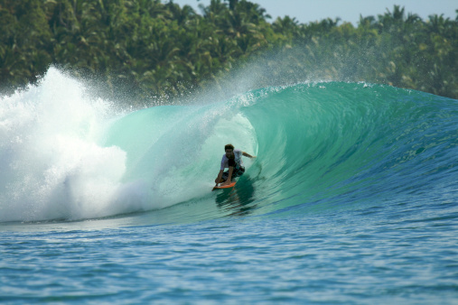 Surfer on orange surfboard riding in barrel on tropical green wave, Mentawai Islands, Indonesia