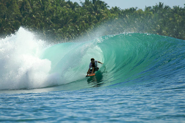 Surfer in barrel on green wave, Mentawai Islands, Indonesia Surfer on orange surfboard riding in barrel on tropical green wave, Mentawai Islands, Indonesia Mentawai Islands stock pictures, royalty-free photos & images