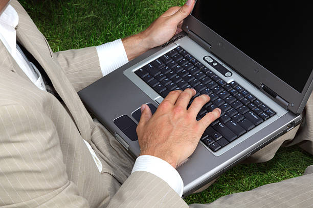 Empresário sentado na grama, usando um computador portátil - fotografia de stock