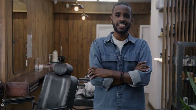 Portrait of joyful guy with stylish haircut standing in barbershop with arms crossed smiling looking at camera