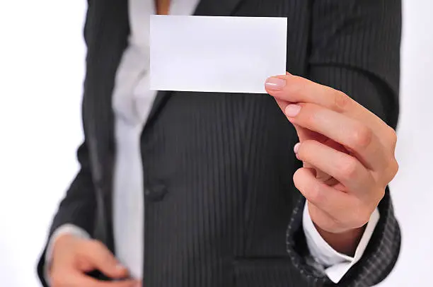 A close up of a business woman demonstrating a blank business card. Her body is blurred but her hand and the business card are in focus.