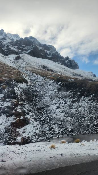 view from below of a rocky mountain with vegetation covered with snow, at the side of the road in the City of Caviahue, province of Neuquén, Argentina stock photo