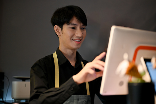 Young Asian male coffee shop owner checking bills for customer with machine. coffee shop worker concept, small business