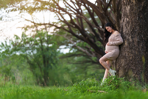 pregnant woman standing and looking her belly in the park
