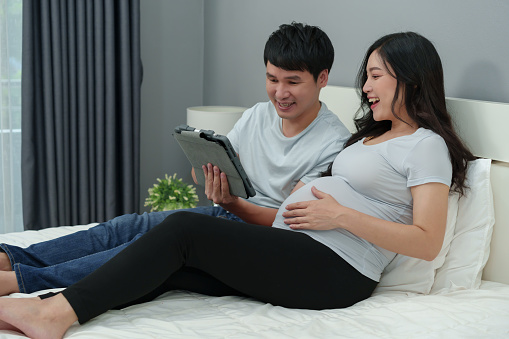 pregnant woman with her husband using digital tablet on a bed