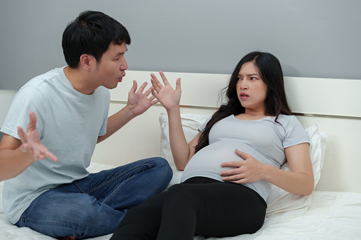 stressed and worried pregnant couple arguing and quarreling on a bed