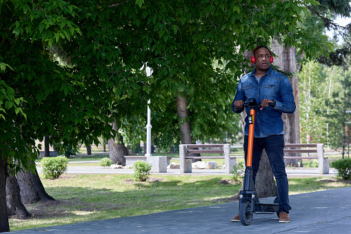 Popular type of environmentally friendly urban transport, an electric scooter is used by an African man for walks. Stylish African-American prepared for a trip to the city park on a scooter