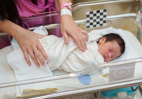 hand of mother putting her newborn baby to sleep in the infant bassinet basket at hospital