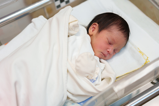 newborn baby laying and sleeping in the infant bassinet basket at hospital