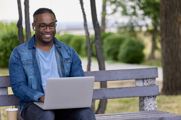 istock Cute black student chats with friends online in chat while sitting on park bench 1515644733