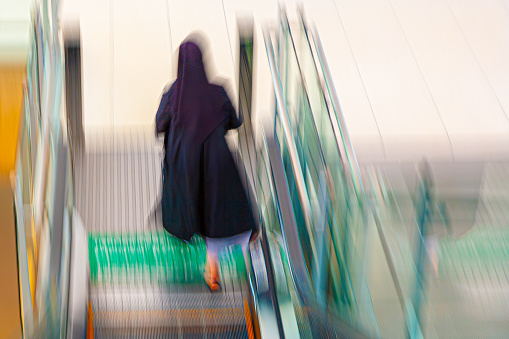 blurred motion - woman in black dress, a nun or a muslima at the moving staircase in blurred motion symbolizing speed and confidence