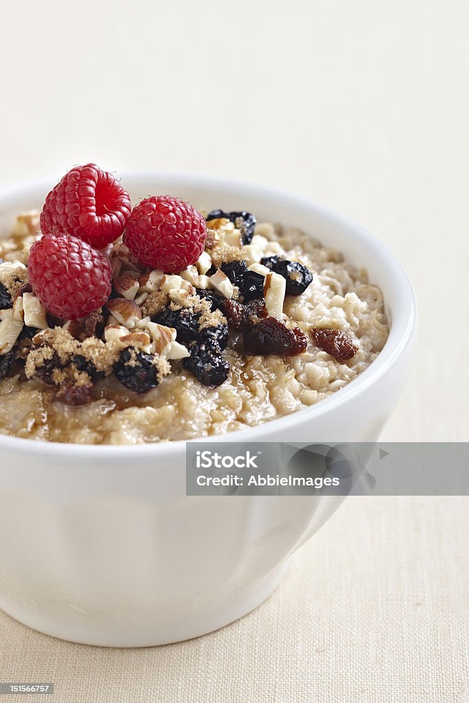 Oatmeal with fruit Nutritious bowl of oatmeal with brown sugar, raisins, nuts and raspberries on top. Almond Stock Photo