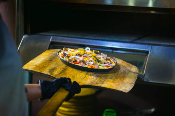 Young woman and chef putting a color full and very complete deliciously italian homemade pizza entering a wood-fired oven for baking. Young woman and chef putting a color full and very complete deliciously italian homemade pizza entering a wood-fired oven for baking. sketch restaurant stock pictures, royalty-free photos & images