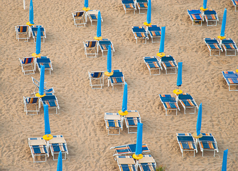 Symmetrically placed beach chairs on clean white sand in Italy. Brands retouched, no further edit. Soft shadows, photo taken from above. Symbolic for holiday.