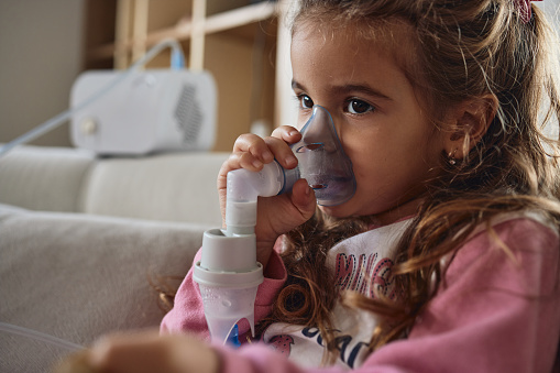 Little girl using nebulizer during inhaling therapy.