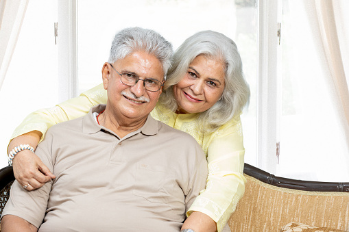Front view of happy senior diverse couple sitting in room at sofa . Authentic Senior Retired Life Concept