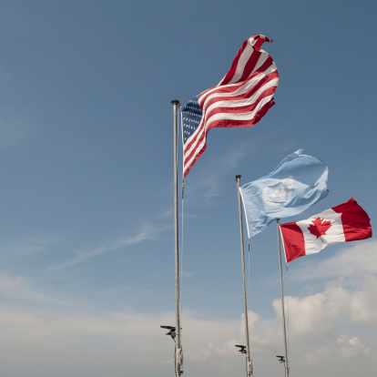The American flag waves next to the United Nations flag which waves next to the Canadian flag.