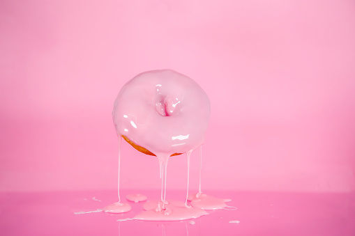 Pink iced donut with pink dripping icing on pink background