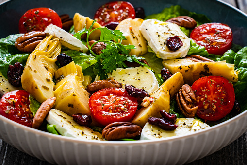 Tasty salad - camembert cheese, artichoke, pecans, tomatoes and fresh leaf vegetables on wooden table