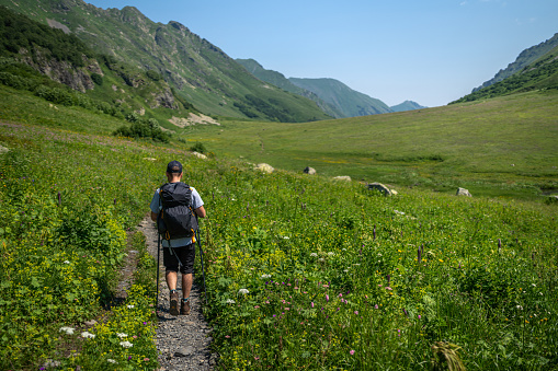Young man hiking at the valley of Caucasus mountains at sunny day