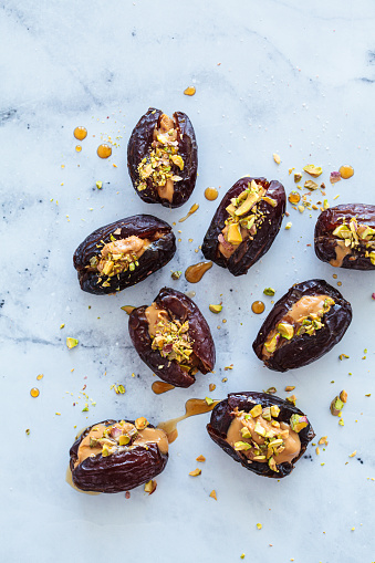Dates stuffed with peanut butter and pistachios on a white marble background. Vegan dessert, healthy snack recipe.