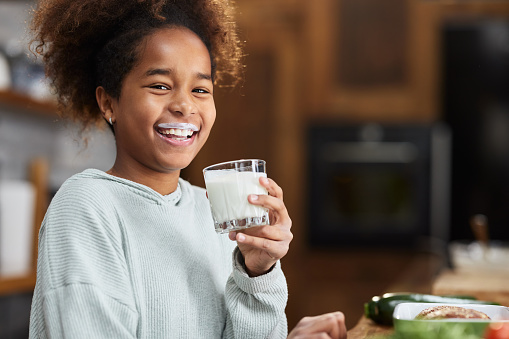 Happy black girl having yogurt mustache during breakfast in dining room and looking at camera.