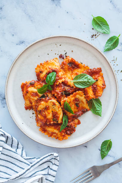 Ravioli with ricotta, tomato sauce and basil, white marble background.