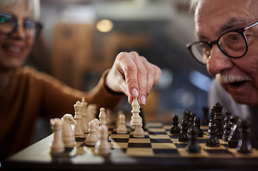 Close up of senior woman making a move in chess while her husband is shocked.
