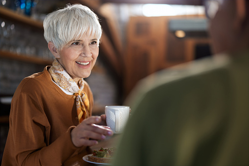 Happy mature woman drinking coffee while talking to her husband during breakfast time in dining room.