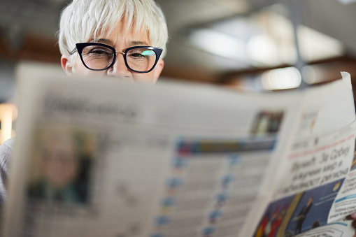 Mature woman enjoying while reading newspapers at home.