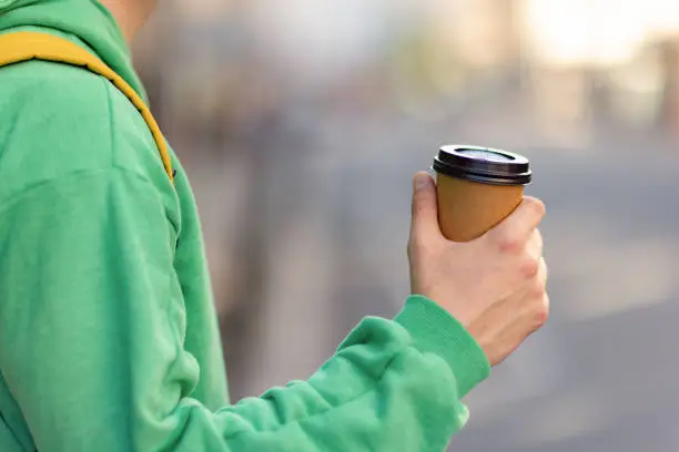 Close up of unrecognizable male tourist holding paper coffee cup on the street.