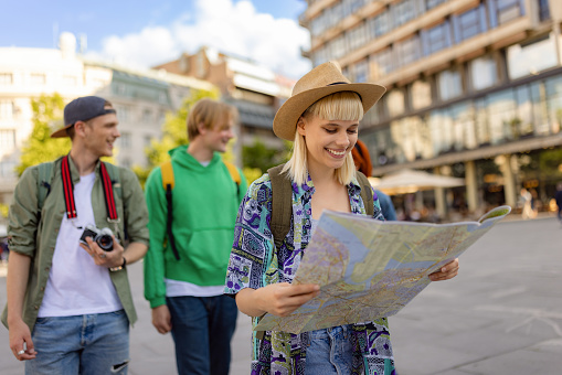Happy female tourist reading a map while exploring the city with her friends.