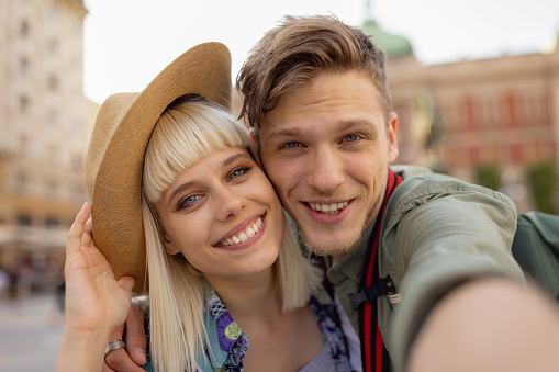 Happy couple of tourists enjoying while taking a selfie in the city and looking at camera.