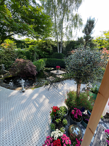 Stock photo showing ornamental Japanese-style garden with outdoor dining area in Spring. Featuring a large expanse of white, interconnecting, white plastic decking tiles, providing a family space for outdoor hardwood seating.