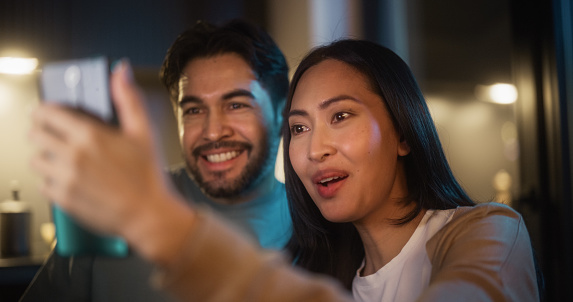 Portrait of a Happy Couple Having Video Call on a Smartphone in a Kitchen at Night. They are Talking and Chatting. Man and Woman Staying Connected to Family and Friends Using Technology and Internet.