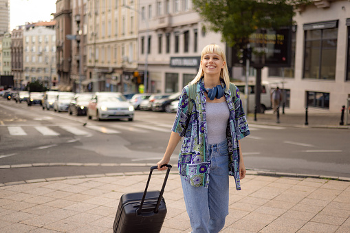 Happy female tourist enjoying while pulling her suitcase on the city street.