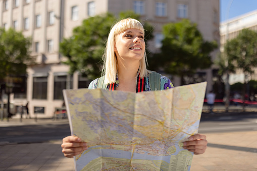 Happy female tourist analyzing a map on the city street.