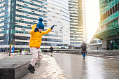 a child in a yellow jacket, blue hat jumps from the curb in the city in winter