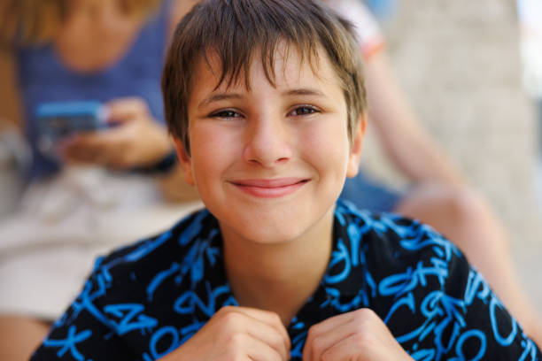 Portrait of preadolescent boy with sweaty hair sitting outdoors and smiling at camera on a hot summer day
